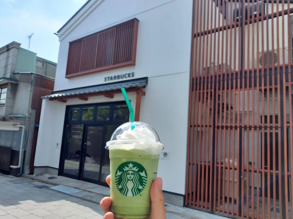 格子窓と白壁が美しいスターバックス店舗前で掲げる抹茶クリームフラペチーノ